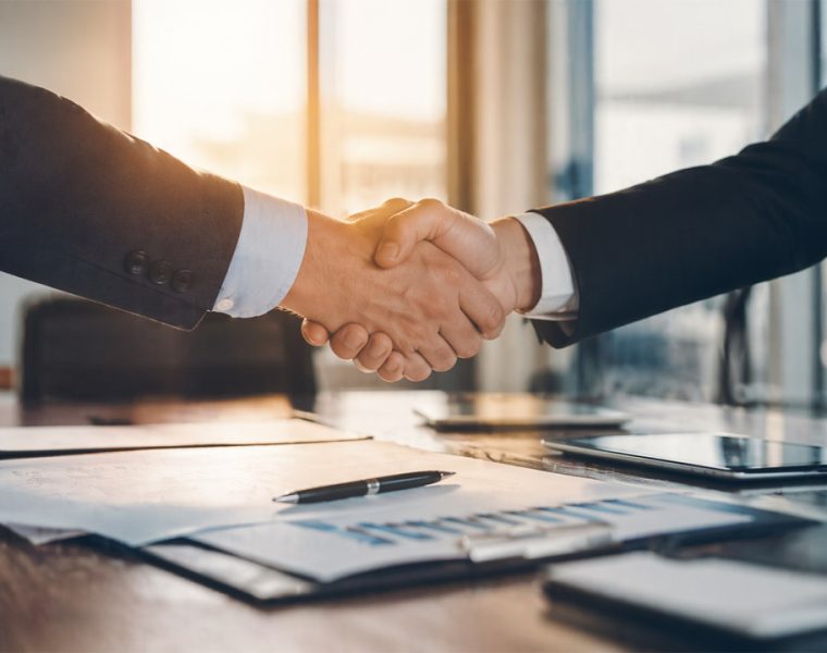 Acquisizione italiana azienda tedesca rappresentata da stretta di mano tra manager in contesto aziendale